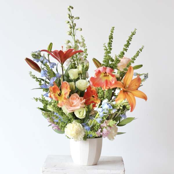 Mixed bouquet of lilies, roses, and blue flowers in a white vase