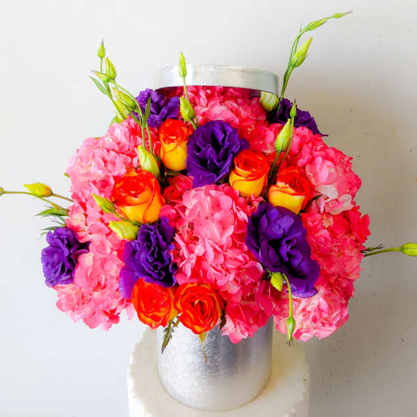 Pink hydrangeas with orange roses and purple blooms in a silver vase