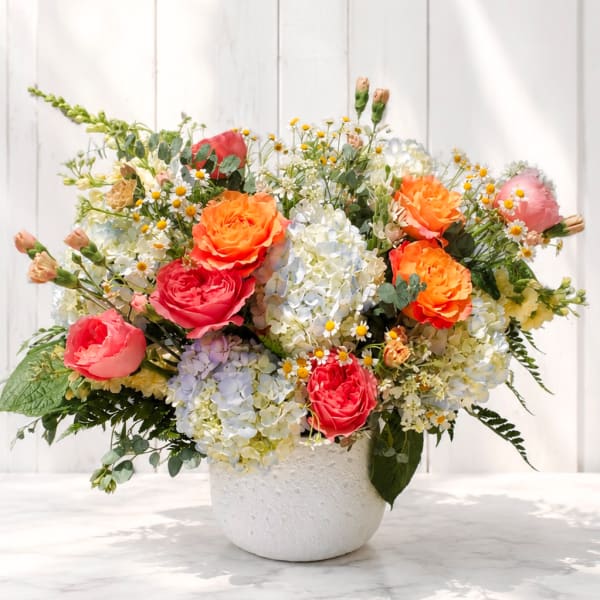 Mixed bouquet of roses, hydrangeas, and daisies in a white vase