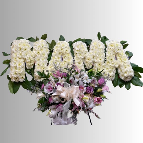 White chrysanthemum floral tribute with pink and purple flowers and a ribbon bow