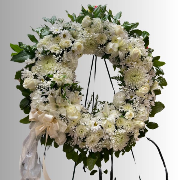 White floral wreath with roses, daisies, and lilies on a stand