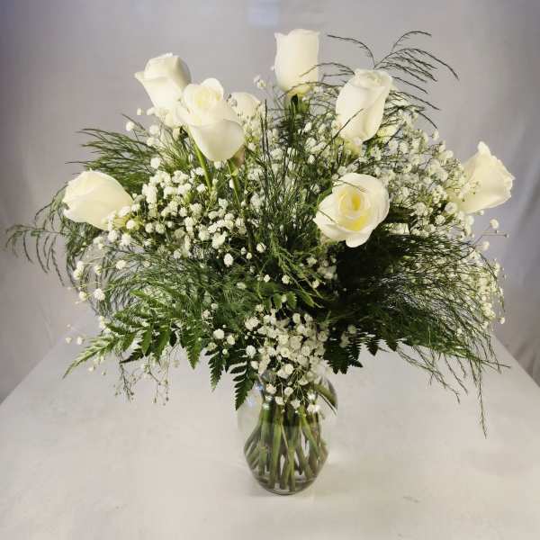 White roses arranged in a clear glass vase with airy filler flowers