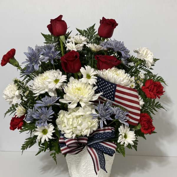 Red roses and white daisies in a white vase with an American flag ribbon