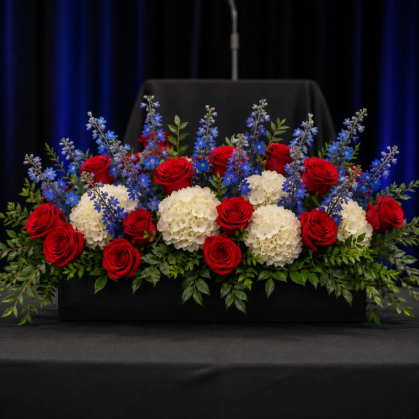 Red roses, white hydrangeas, and blue flowers in a black rectangular container