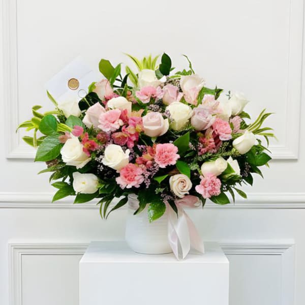 Pink and white bouquet in a white vase with a ribbon