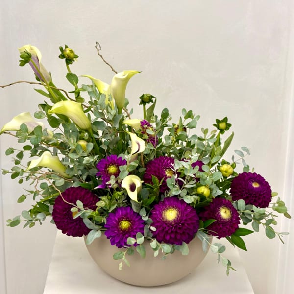 Purple dahlias and pale calla lilies arranged in a white bowl vase