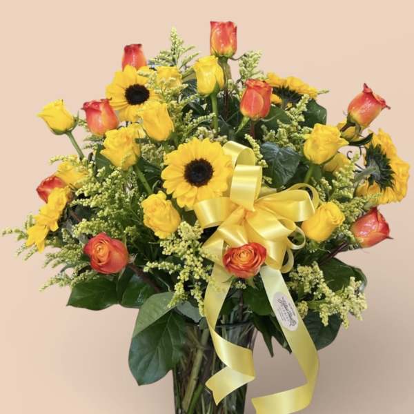 Sunflowers and orange-yellow roses in a clear glass vase with a yellow ribbon