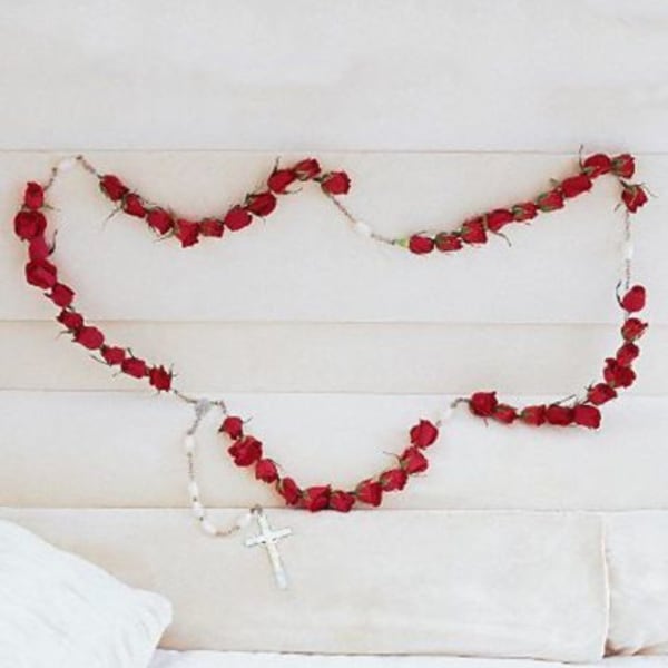 Red rose garland draped across a white upholstered headboard with a rosary hanging below