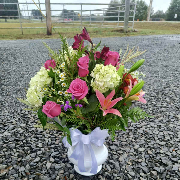 Pink roses and lilies arranged in a white vase with a lavender ribbon