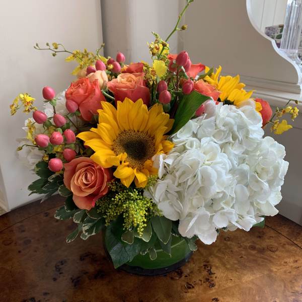 Mixed bouquet with sunflowers, coral roses, white hydrangea, and pink buds in a green vase