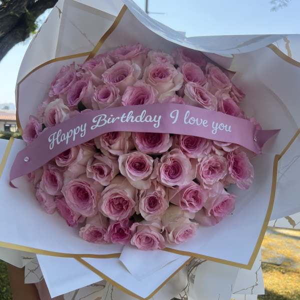 Bouquet of pink roses wrapped in white paper with a birthday ribbon