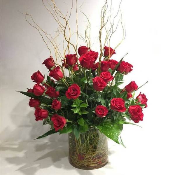 Red roses arranged in a clear glass vase with tall curly branches