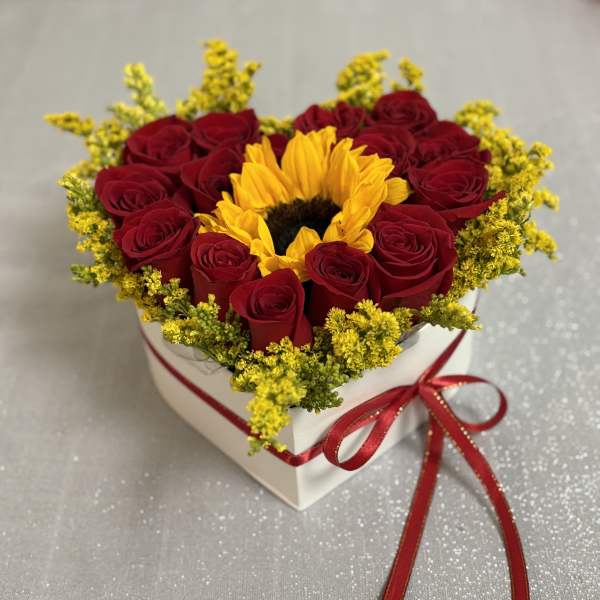 Heart-shaped box of red roses with a sunflower center and red ribbon
