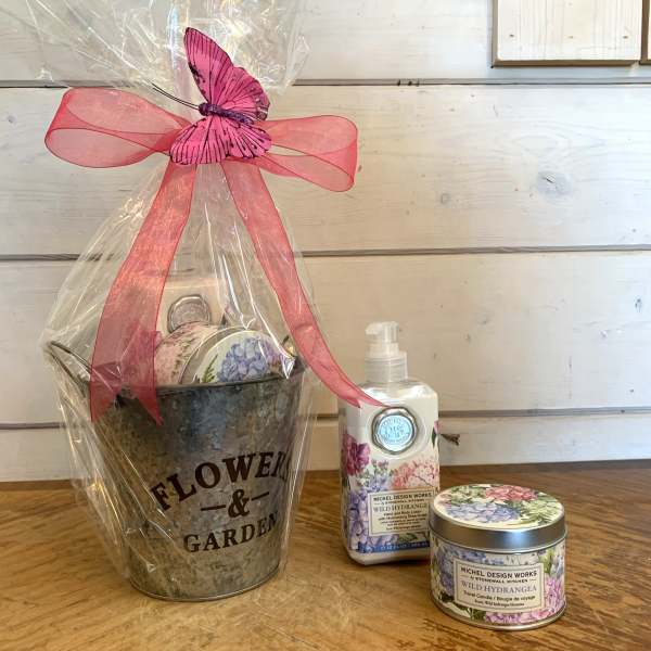 Gift basket with a flower garden bucket, lotion, and candle tied with a pink ribbon