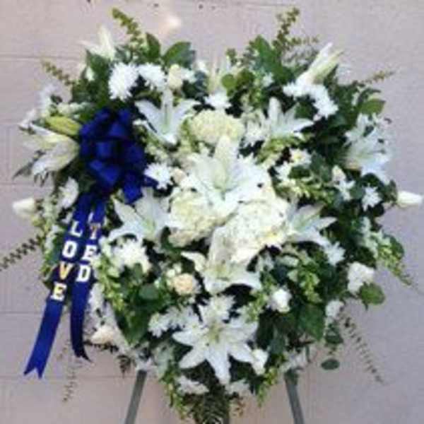 White funeral spray with lilies and a blue ribbon