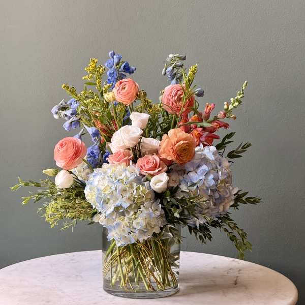 Mixed bouquet in a clear glass vase with pastel pink, blue, and white blooms