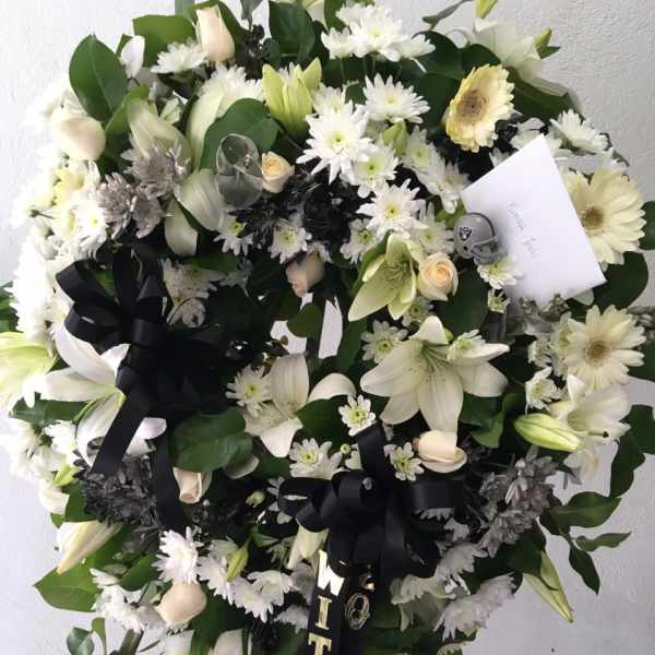 Large white floral wreath with black ribbons on a stand