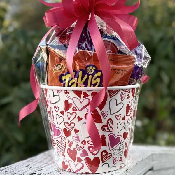 Heart-patterned gift bucket filled with candy and topped with a pink ribbon bow