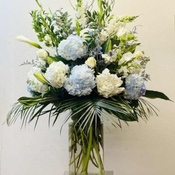 Tall white and pale blue floral arrangement in a glass vase
