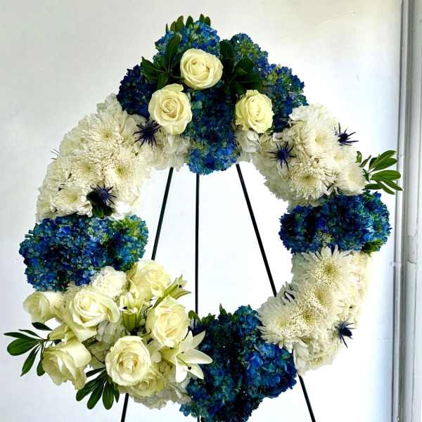 Circular floral wreath with white roses, blue hydrangeas, and white chrysanthemums on a stand