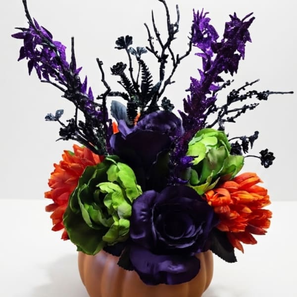 Purple, green, and orange floral arrangement in a pumpkin-shaped container