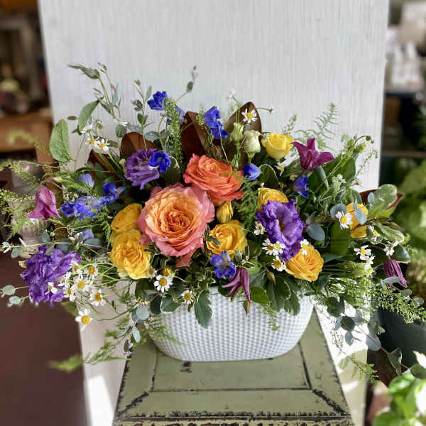 Mixed bouquet of roses, lisianthus, and small daisies in a white vase