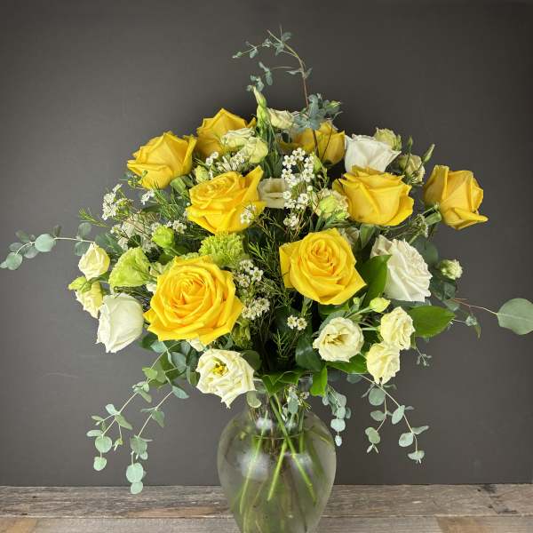 Yellow and white roses in a clear glass vase with airy filler flowers