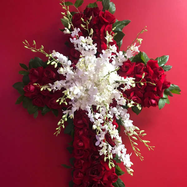 Cross-shaped floral arrangement of red roses and white orchids on an easel