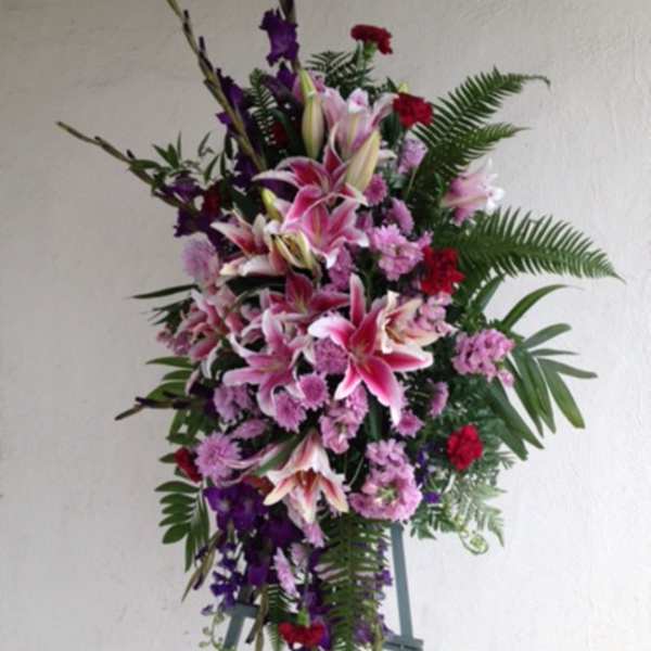 Tall standing floral spray with pink lilies and purple flowers on an easel