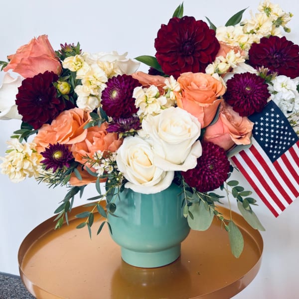Mixed bouquet of roses and burgundy dahlias in a teal vase with an American flag