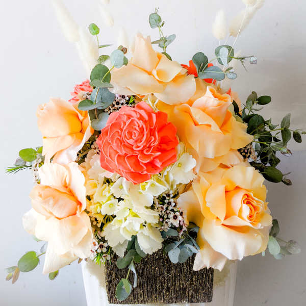 Peach and coral roses with white filler flowers in a square container