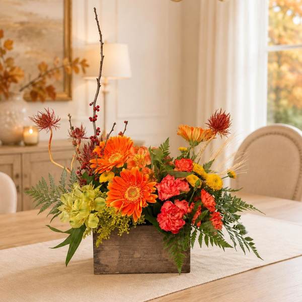 Orange and red floral arrangement in a wooden box on a dining table