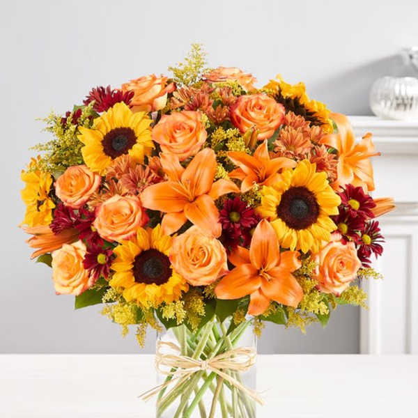 Bouquet of orange roses, sunflowers, and lilies in a glass vase