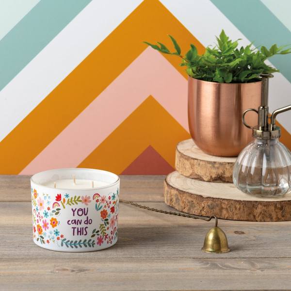 Decorative candle with floral print and a copper planter with greenery