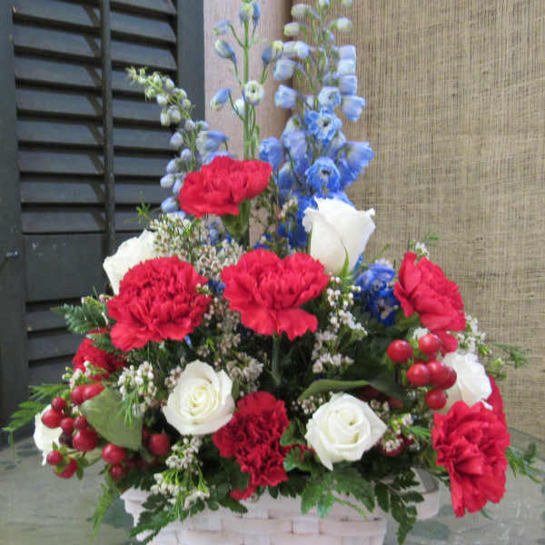 Basket arrangement of red carnations, white roses, and blue delphinium