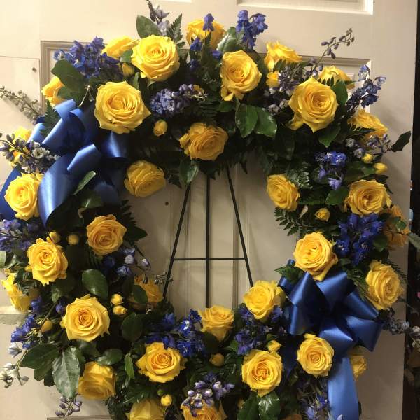 Yellow rose wreath with blue ribbon accents on a stand