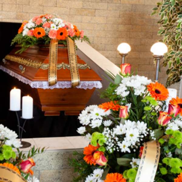Funeral casket with orange and white floral sprays and candles