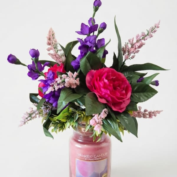 Pink and purple floral arrangement in a glass candle jar