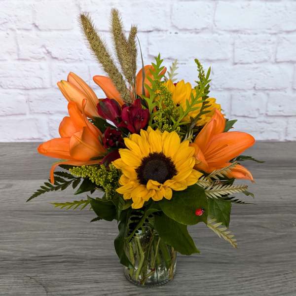 Bouquet of sunflowers, orange lilies, and burgundy blooms in a glass vase