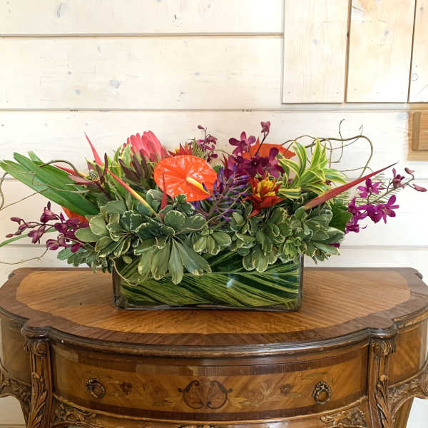 Tropical flower arrangement in a rectangular glass vase with orange and purple blooms