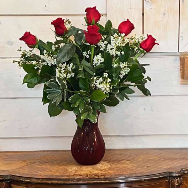 Red roses arranged in a burgundy vase with white filler flowers