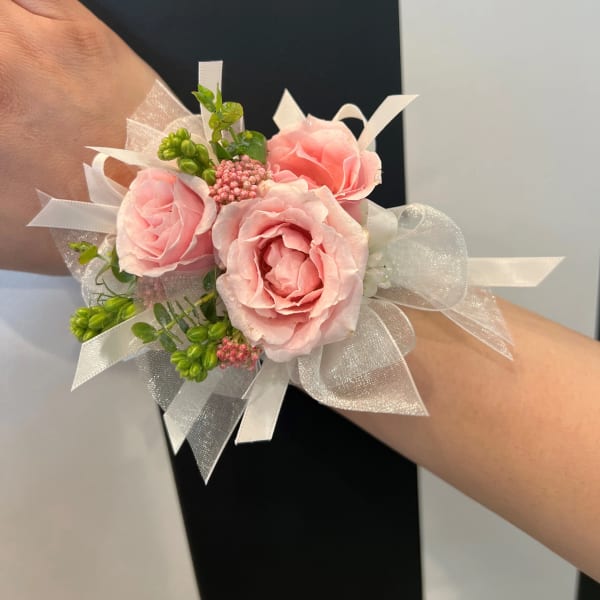 Pink rose wrist corsage with white ribbon and green accents