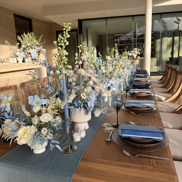 Blue and white floral centerpieces on a long dining table with candles and place settings