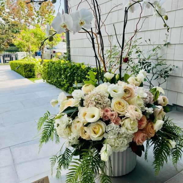 Large white floral arrangement with orchids and roses in a metal container