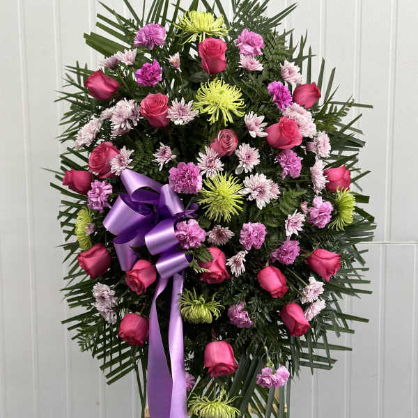 Standing floral wreath with pink roses, chrysanthemums, and a purple ribbon