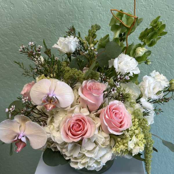 Pink roses and white orchids in a low vase with white hydrangea