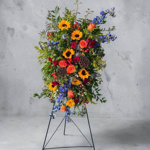 Tall standing floral spray with sunflowers, roses, and blue flowers on a metal easel