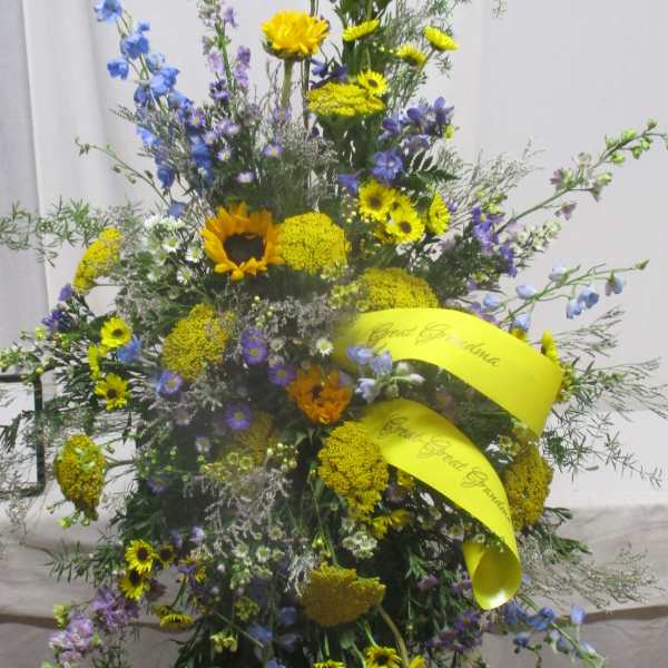 Tall standing floral spray with yellow and blue flowers on a black easel