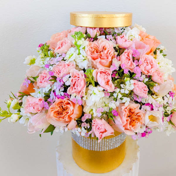 Pink and white floral arrangement in a gold hatbox with a rhinestone band