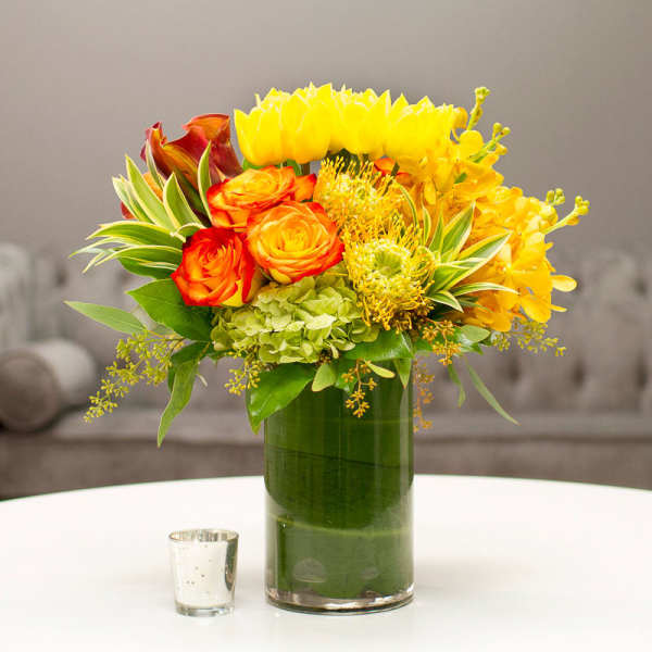 Bright yellow and orange floral arrangement in a tall glass vase